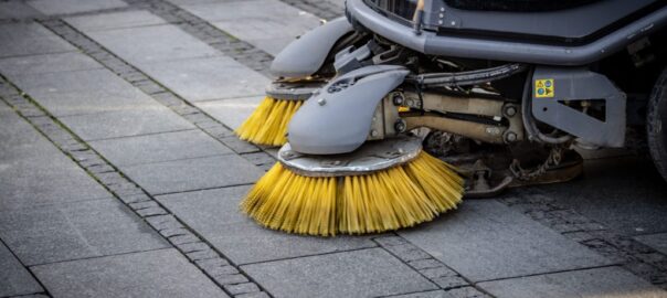 Close-up view of a road sweeper's yellow brushes on a paved street.